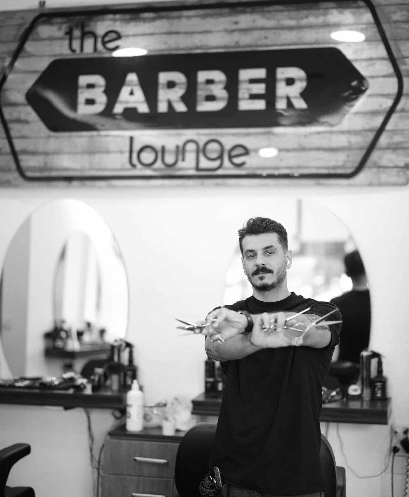 A barber holding his shears beneath The Barber Lounge sign